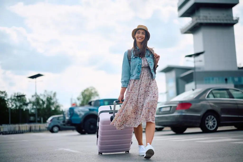 VMXxKluA - Fusion Parking A young lady walking through a parking lot with a suitcase feeling safe and happy with her adventure ahead because they have a solid parking lot maintenance plan.